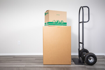 Cardboard moving boxes on hand truck indoors, ready for transportation.