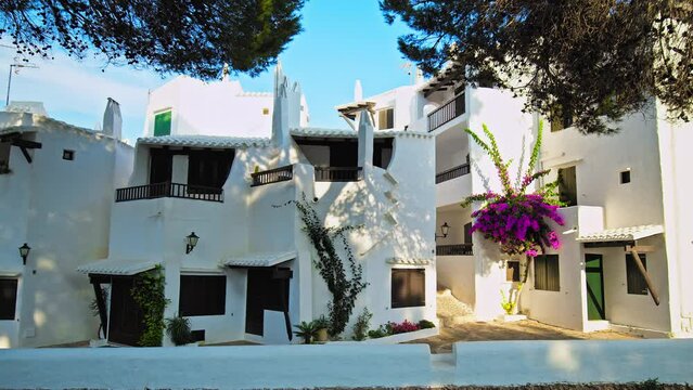 Scenic view of Binibeca Village with whitewashed houses and tropical green trees. Relaxing tourist resort Binibeca Vell with narrow streets and a calm cove - paradise-like town in Menorca, Spain.