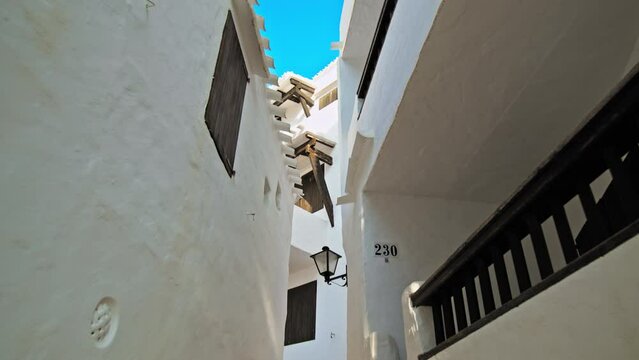 Narrow Whitewashed Streets in a tourist resort Binibeca Vell in Menorca, Spain. Beautiful small village town on the Balearic Islands with traditional brown wooden windows and doors in Europe.