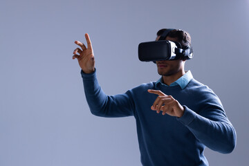 Biracial businessman using vr headset and pointing with fingers on grey background