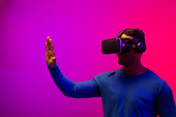 Biracial businessman using vr headset and pointing with hand on neon pink to purple background
