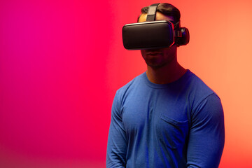 Biracial businessman using vr headset on neon pink to orange background
