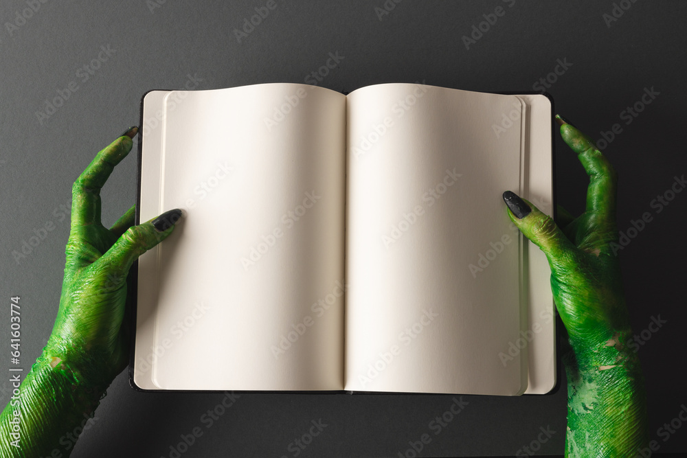 Wall mural green monster hands holding notebook with copy space on grey background