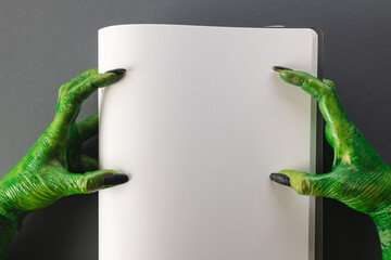 Green monster hands holding notebook with copy space on grey background