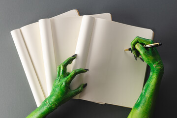 Green monster hands writing on notebook with copy space on grey background