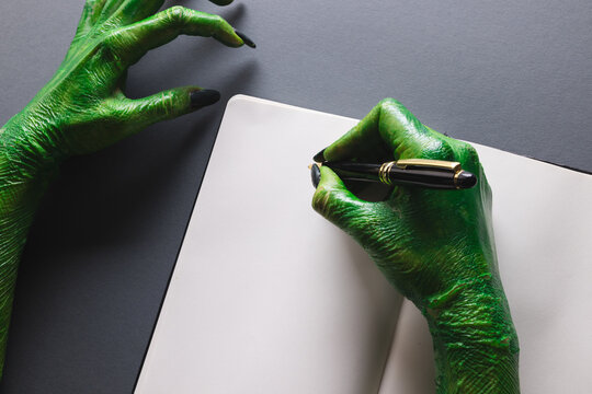 Green monster hands writing notebook with copy space on grey background