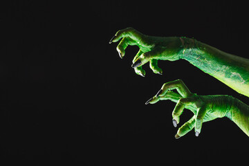 Green monster hand with black nails reaching on grey background