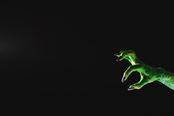 Green monster hand with black nails reaching on black background