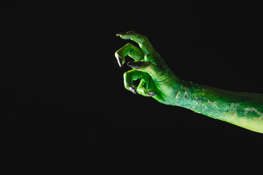 Green monster hand with black nails reaching on grey background
