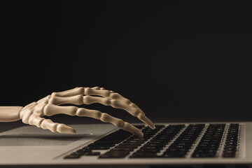 Plastic skeleton hand on laptop keyboard with copy space on black background