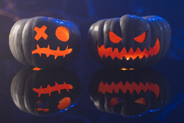 Fototapeta premium Two black carved pumpkins faces on blue background