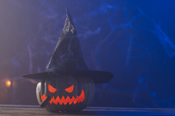 Fototapeta premium Carved pumpkin wearing witch hat with copy space on blue background