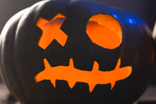 Fototapeta Carved pumpkin face illuminating with orange light on black background