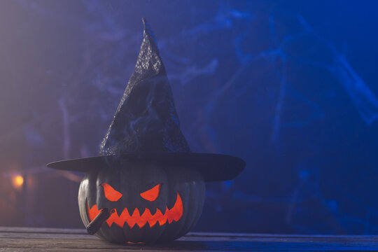 Fototapeta Carved pumpkin wearing witch hat with copy space on blue background