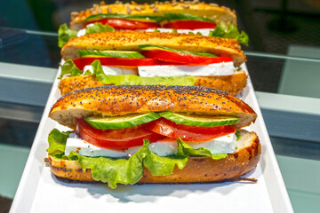 Showcase with one vegetable vegan sandwich in a cafe. Bread for take away with cheese, tomatoes, cucumbers and green leaf and salad - obrazy, fototapety, plakaty