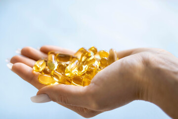 Close-up medicine yellow transparent pills, omega 3 fish oil capsules, vitamin D. Many yellow transparent capsules in hand close-up. The concept of health, vitamins, and medicine