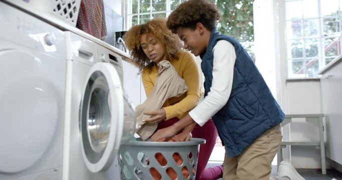 Happy african american mother and son doing laundry together, slow motion