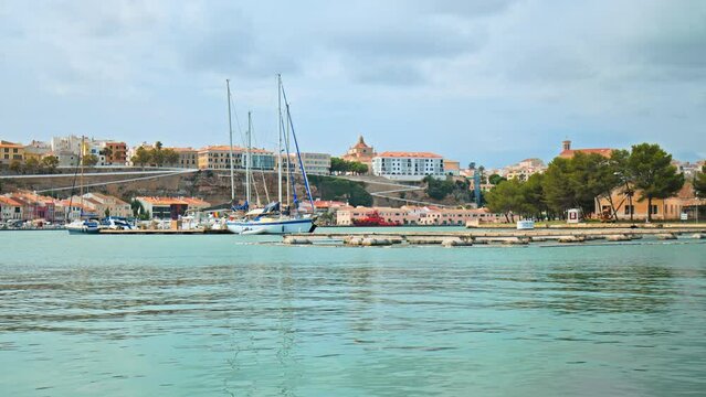 Boats and ships floating by the seashore of Mahon City in Menorca, Spain in 4K. Sea Life concept on the Balearic Islands with sailing vessels and colourful Spanish houses.