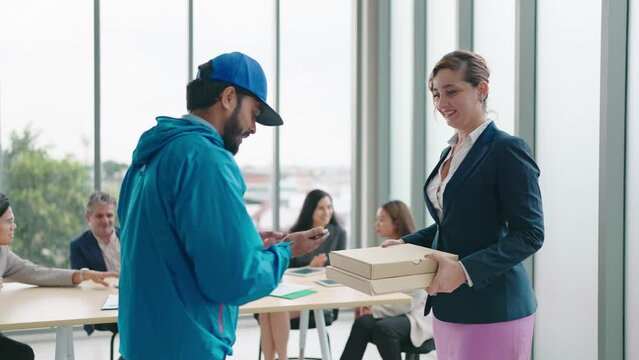 Woman manager taking pizza box from food delivery man for enjoy lunch together with colleagues in meeting room at office.Women manager orders food online to team. Delivery food concept