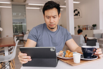 Asian man sitting working drinking coffee with tablet at cafe.