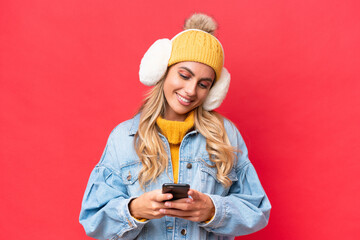 Young pretty Uruguayan woman wearing winter muffs isolated on red background background sending a...