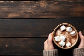 Female hands holding a cup of hot cocoa with marshmallows on wooden background. Top view with copy space