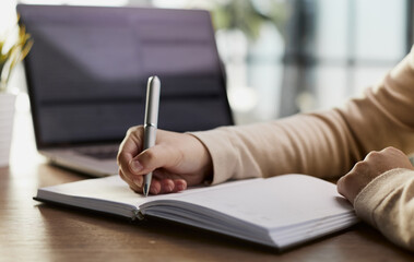 Close up of man hands writing in spiral notepad placed on wooden desktop with various items