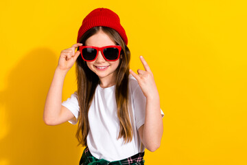 Photo portrait of charming little girl sunglass showing rock gesture sign dressed stylish white garment isolated on yellow color background