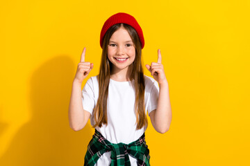 Obraz na płótnie Canvas Photo portrait of charming schoolgirl pointing fingers up empty space wear trendy white garment isolated on yellow color background