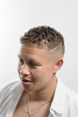 Candid portrait of  a woman standing in a studio, against a white backdrop. She is in conversation, and only loosely paying attention to the camera. She has a fade haircut, expressing her butch style.