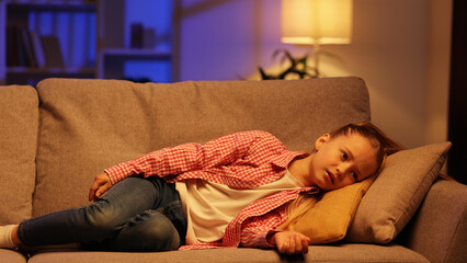 Tired little girl slumps on couch feeling listless. Feeling depressed, lack of motivation, sadness,...
