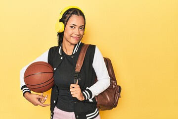 Indonesian student girl holding basketball on a yellow studio background