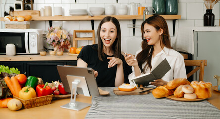 Two beautiful woman in the kitchen in an apron, fresh vegetables on the desk, writes down her favorite recipes, comes up with ideas for dishes