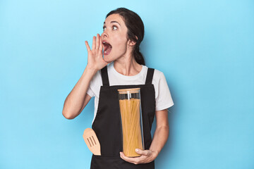 Chef woman with pasta jar on blue shouting and holding palm near opened mouth.