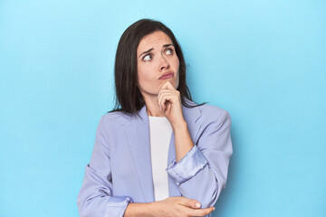 Woman in blue blazer on blue background thinking and looking up, being reflective, contemplating, having a fantasy.