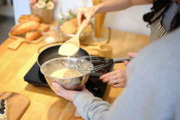 Young couple preparing breakfast, pouring batter for making pancakes with a ladle into a frying pan