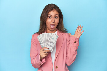 Teen girl in pink, flaunting a handful of dollar bills receiving a pleasant surprise, excited and...