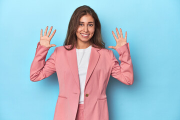 Teen girl in chic pink suit on a blue background showing number ten with hands.