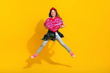 Full size photo of adorable schoolgirl jump spread legs hold heart pinata dressed stylish white outfit isolated on yellow color background