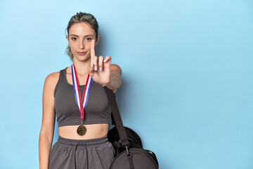 Athlete with medal and sports backpack showing number one with finger.