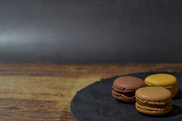 Macarons in brown and yellow tones, on a slate plate, on a wooden table