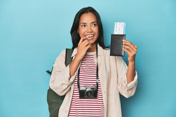 Filipina with camera, tickets, backpack on blue relaxed thinking about something looking at a copy space.