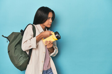 Filipina promoting excursions with lantern and backpack on blue studio