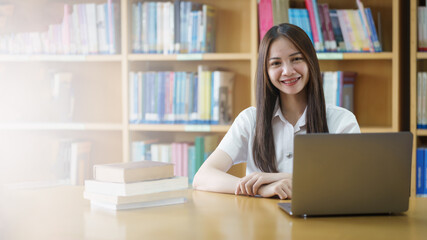 Fototapeta premium Portrait of an Asian girl college student studying in library doing project assignment and preparing for examination