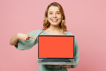 Young smiling happy IT woman wears casual clothes hold use work on point finger on laptop pc...