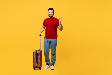 Traveler happy fun Indian man wear red casual clothes hold bag point aside isolated on plain yellow...