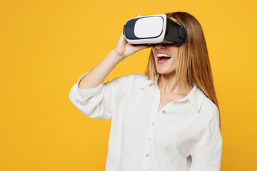 Young smiling cheerful saisfied cool caucasian happy woman she wears white shirt casual clothes watching in vr headset pc gadget isolated on plain yellow background studio portrait. Lifestyle concept.
