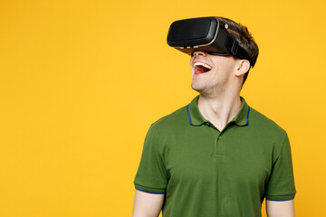 Young surprised amazed cheerful fun cool caucasian happy man wears green t-shirt casual clothes watching in vr headset pc gadget isolated on plain yellow background studio portrait. Lifestyle concept.