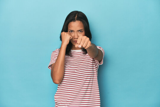 Filipina young woman on blue studio throwing a punch, anger, fighting due to an argument, boxing.