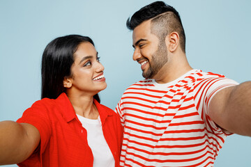 Obraz premium Close up young couple two friends family Indian man woman wear red casual clothes t-shirt together do selfie shot pov on mobile cell phone hugging isolated on pastel plain blue cyan color background.